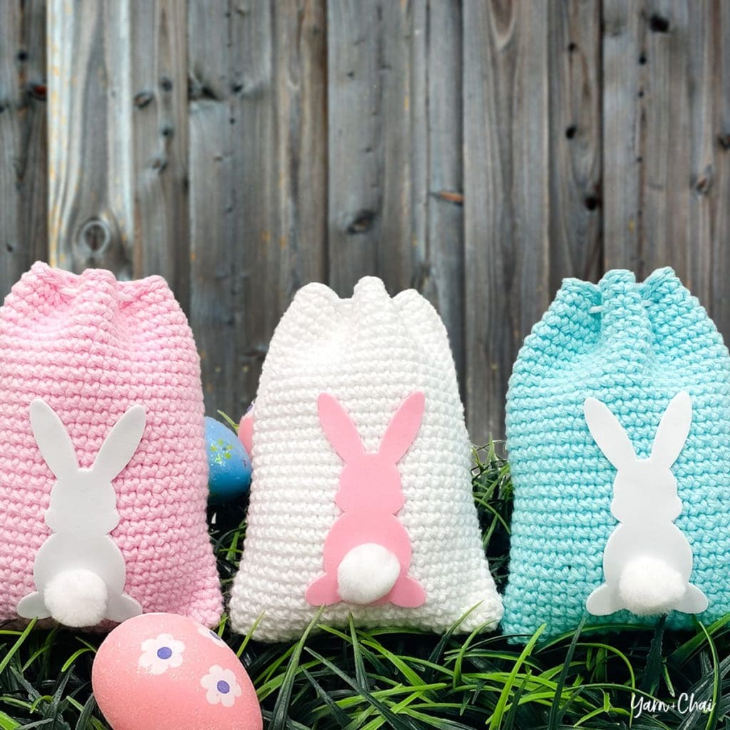 Three easter bunny treat bags surrounded by grass and colorful eggs